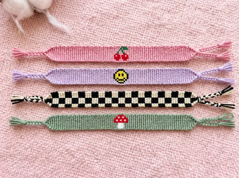 Alpha friendship bracelets with cherry, smiley face, checkerboard and mushroom designs on a pink blanket