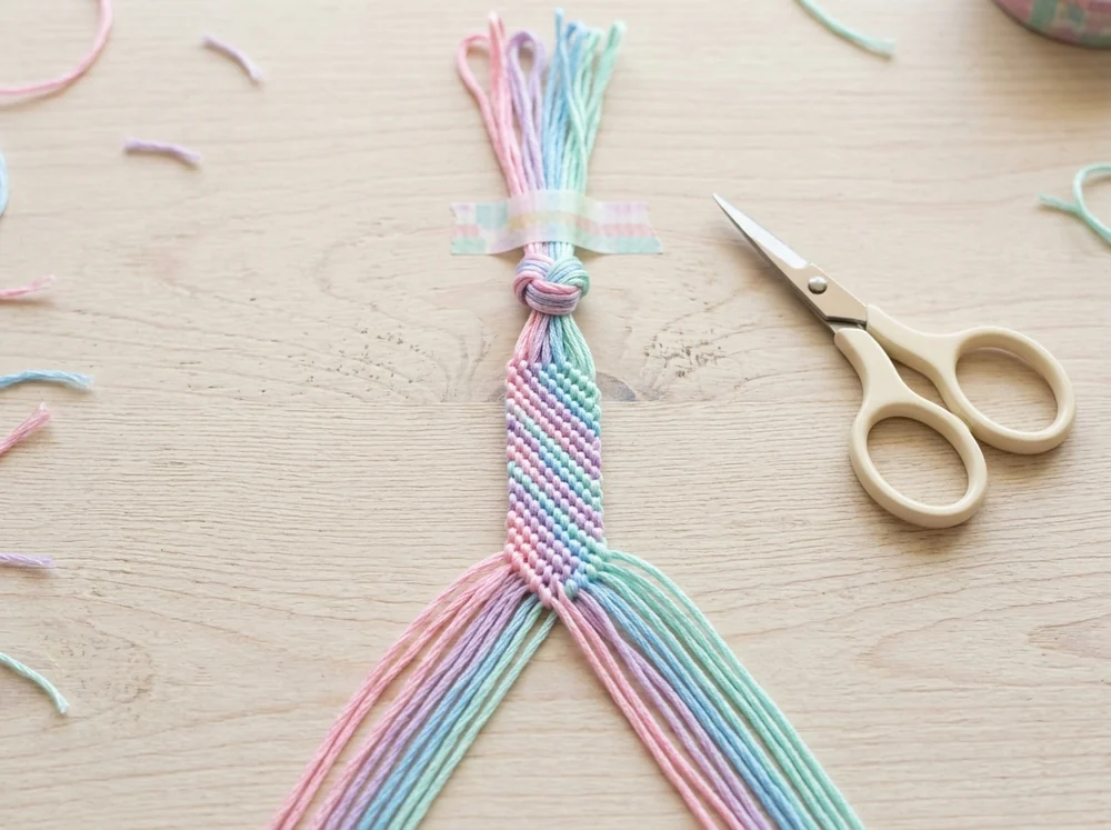 How to start a friendship bracelet: embroidery floss knotted and taped to a table in pattern order